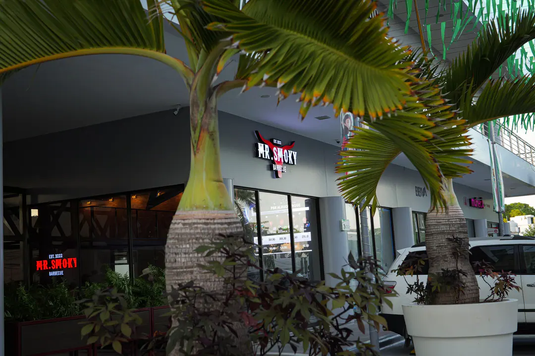 Fachada de Mr. Smoky entre palmeras, junto a BBVA en Centro Esmeralda