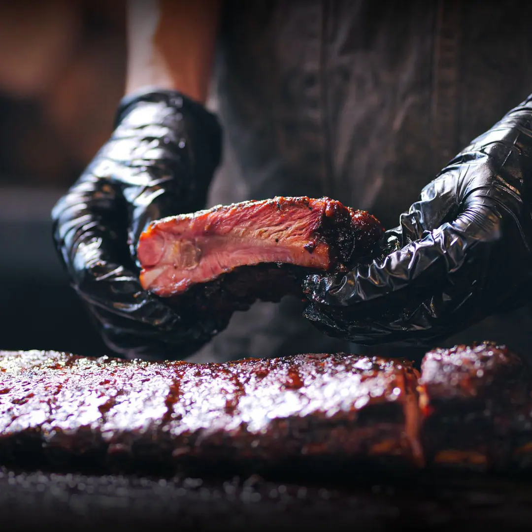 Costilla de cerdo ahumada sostenida por manos con guantes negros
